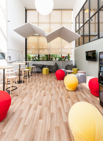 Espace détente aménagé pour savourer un café, avec le choix entre des tabourets et une table haute ou des poufs Take Ten pour une expérience de pause confortable et informelle.