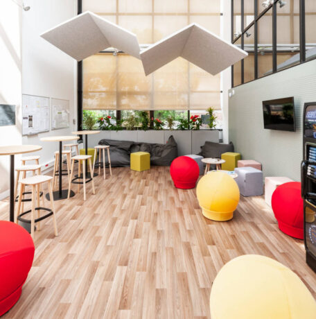 Espace détente aménagé pour savourer un café, avec le choix entre des tabourets et une table haute ou des poufs Take Ten pour une expérience de pause confortable et informelle.