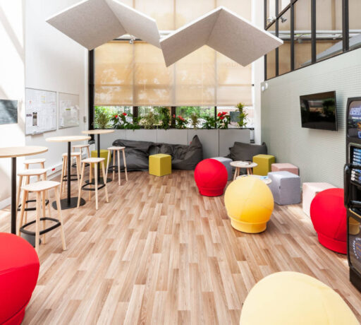 Espace détente aménagé pour savourer un café, avec le choix entre des tabourets et une table haute ou des poufs Take Ten pour une expérience de pause confortable et informelle.