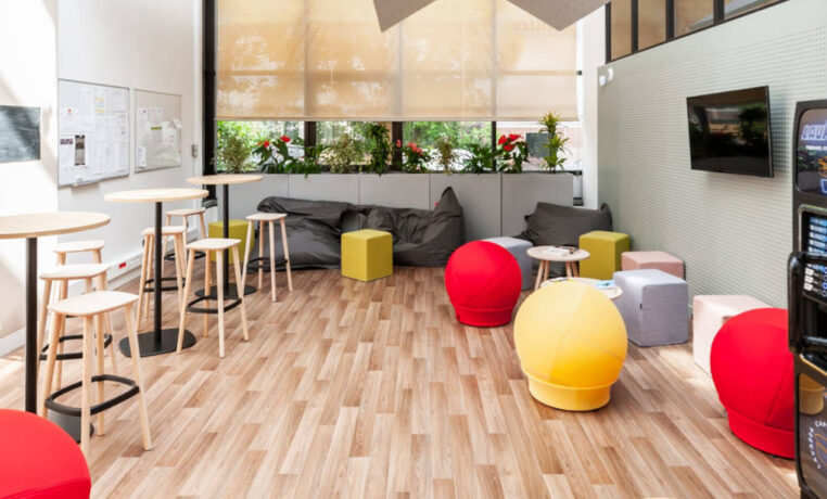 Espace détente aménagé pour savourer un café, avec le choix entre des tabourets et une table haute ou des poufs Take Ten pour une expérience de pause confortable et informelle.