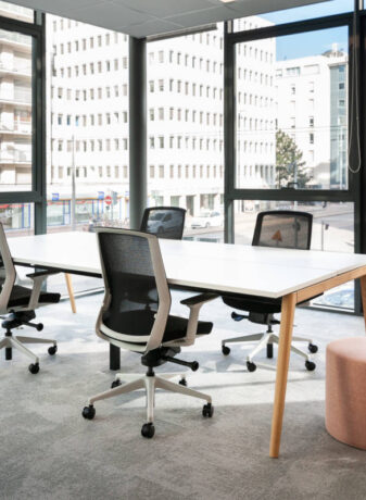 Bureau équipé d'une table Woodesk accompagnée de quatre sièges ergonomiques J1 et d'un pouf, offrant un espace de travail fonctionnel et confortable pour des sessions prolongées.