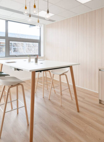 Espace de collaboration en bois avec une table haute et des tabourets multicolores, offrant un cadre dynamique et stimulant pour des sessions de travail en groupe.