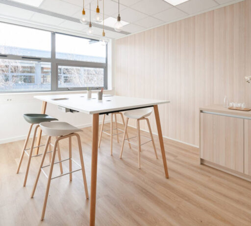 Espace de collaboration en bois avec une table haute et des tabourets multicolores, offrant un cadre dynamique et stimulant pour des sessions de travail en groupe.
