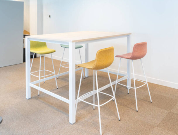 Zone de travail collaboratif chez Dipra, équipée d'une table haute et de tabourets colorés qui permettent une configuration flexible pour les projets d'équipe et les réunions informelles.