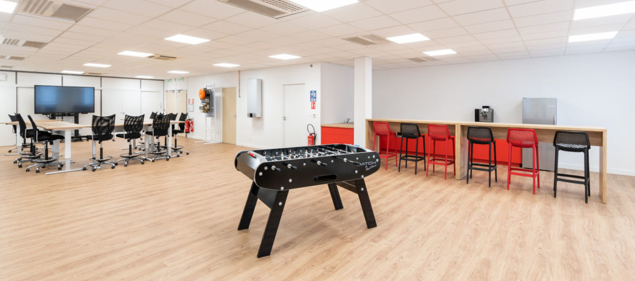 Coin café chez Ariston, équipé d'un baby-foot pour offrir aux collaborateurs un moment de détente ludique pendant leurs pauses, ainsi que des tables hautes et des tabourets pour les repas et les échanges informels.