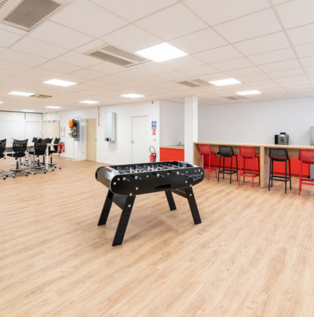 Coin café chez Ariston, équipé d'un baby-foot pour offrir aux collaborateurs un moment de détente ludique pendant leurs pauses, ainsi que des tables hautes et des tabourets pour les repas et les échanges informels.
