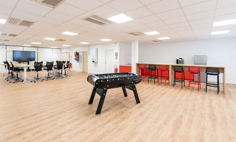 Coin café chez Ariston, équipé d'un baby-foot pour offrir aux collaborateurs un moment de détente ludique pendant leurs pauses, ainsi que des tables hautes et des tabourets pour les repas et les échanges informels.