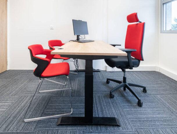 Bureau fermé chez Ariston équipé d'un bureau réglable en hauteur, d'un siège ergonomique et de chaises Joky à piètement luge, offrant un espace de travail privé et flexible.