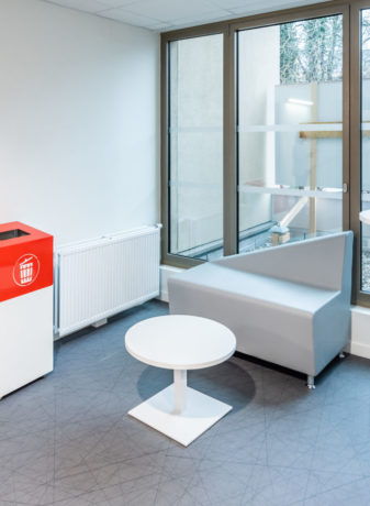 Espace de pause chez Département du Rhône aménagé avec un canapé confortable, une table basse Linéa, une table haute Linéa et un container poubelle, idéal pour les moments d'attente.