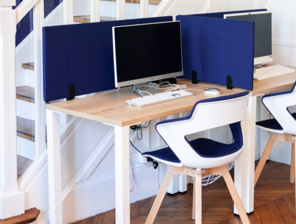 Zone de travail chez Léa Solidarité Femmes avec deux tables équipées d'ordinateurs, séparées par des séparateurs acoustiques, et des chaises Joky à piètement en bois, favorisant la concentration et le confort.