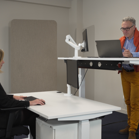 Aménagement ergonomique avec deux bureaux réglables en hauteur Dyna, illustrant les positions assise et debout au travail.