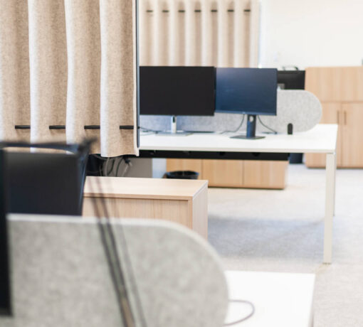 Open space moderne aménagé avec plusieurs bureaux, comprenant des postes de travail doubles et séparés par des cloisons centrales, ainsi que des pôles de bureaux délimités par des séparateurs pour favoriser à la fois la collaboration et l’intimité des collaborateurs.